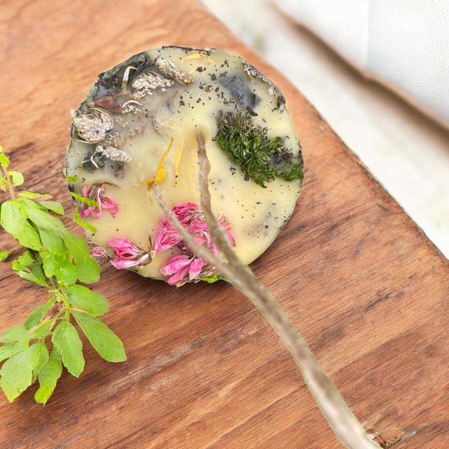 Handmade beeswax Earth candle with herbs and flowers on wooden board